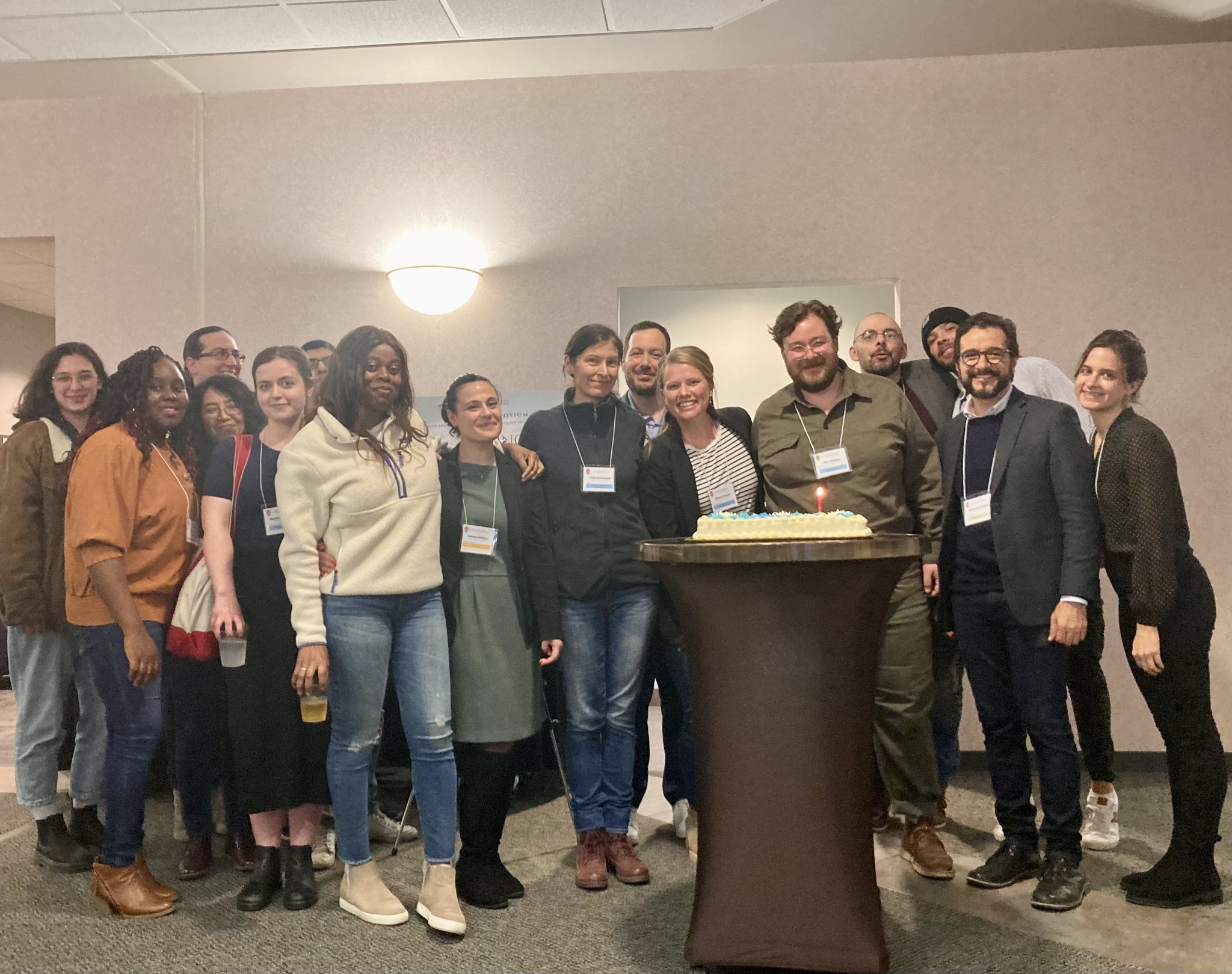 A group of FRIT students and staff smile as they pose for a picture. A birthday cake is in front of them, with a single candle lit.